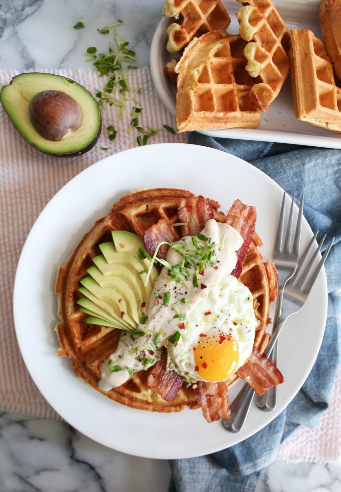 A Belgian waffle with bacon, a fried egg and avocado, more waffles on the side