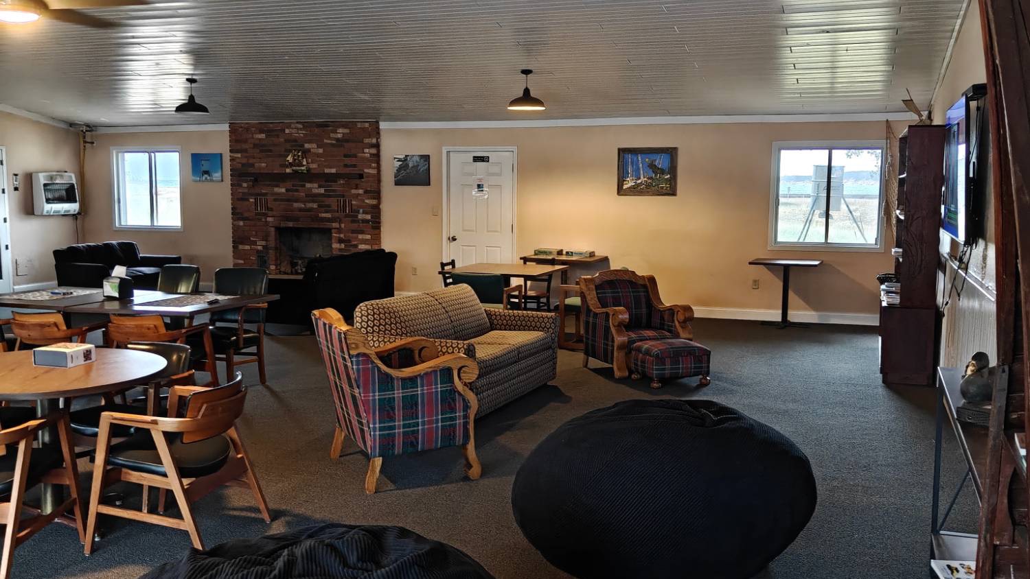 The Captain's Club: a brick fireplace, a sofa and plaid armchairs, game tables and a window on the bay