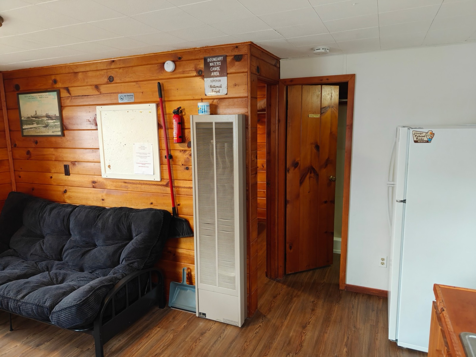 The futon, the wall heater, the door to the bedroom and the fridge
