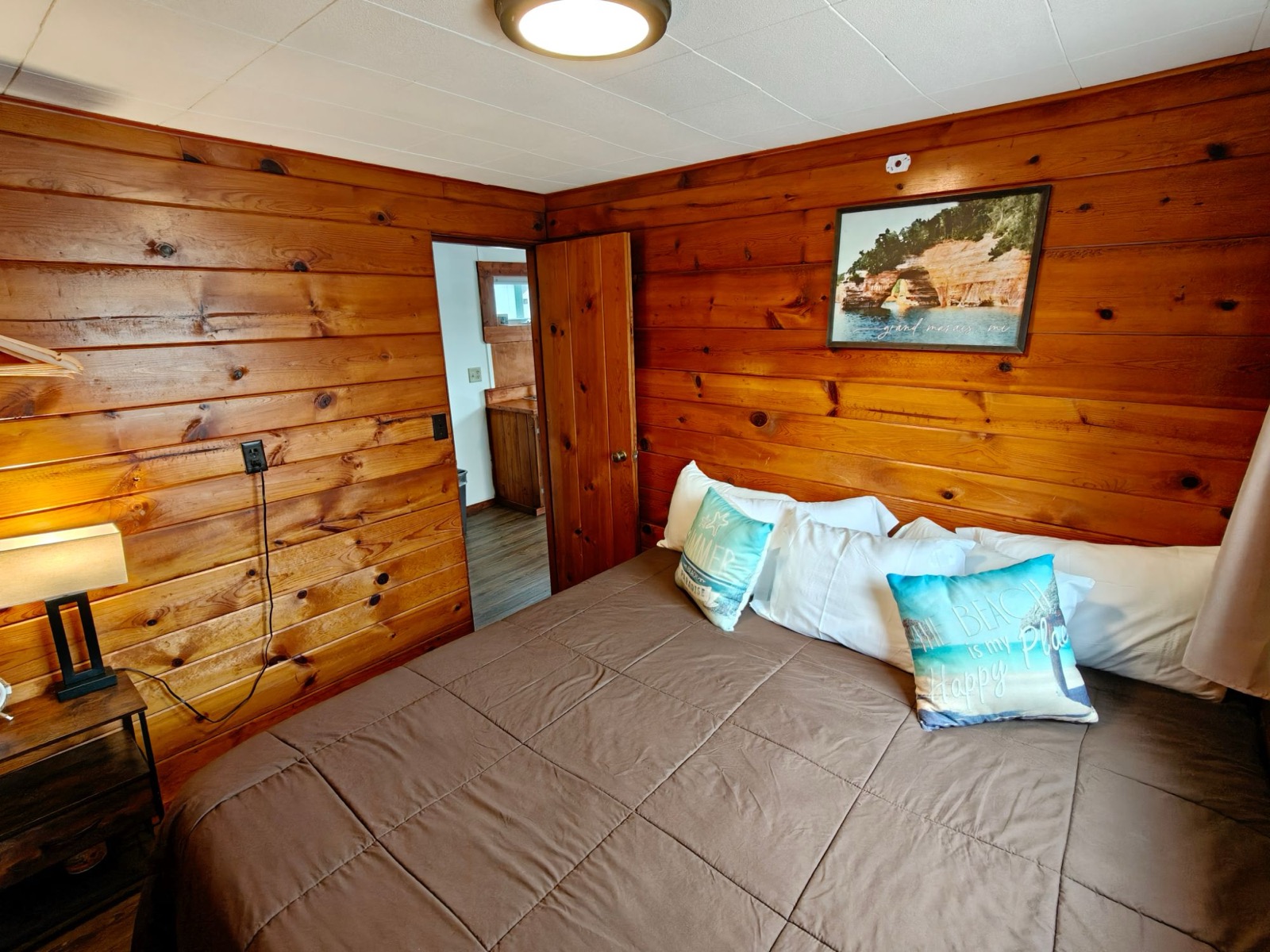 The cottage bedroom: a king bed with beach cushions, knotty pine walls and a Pictured Rocks print