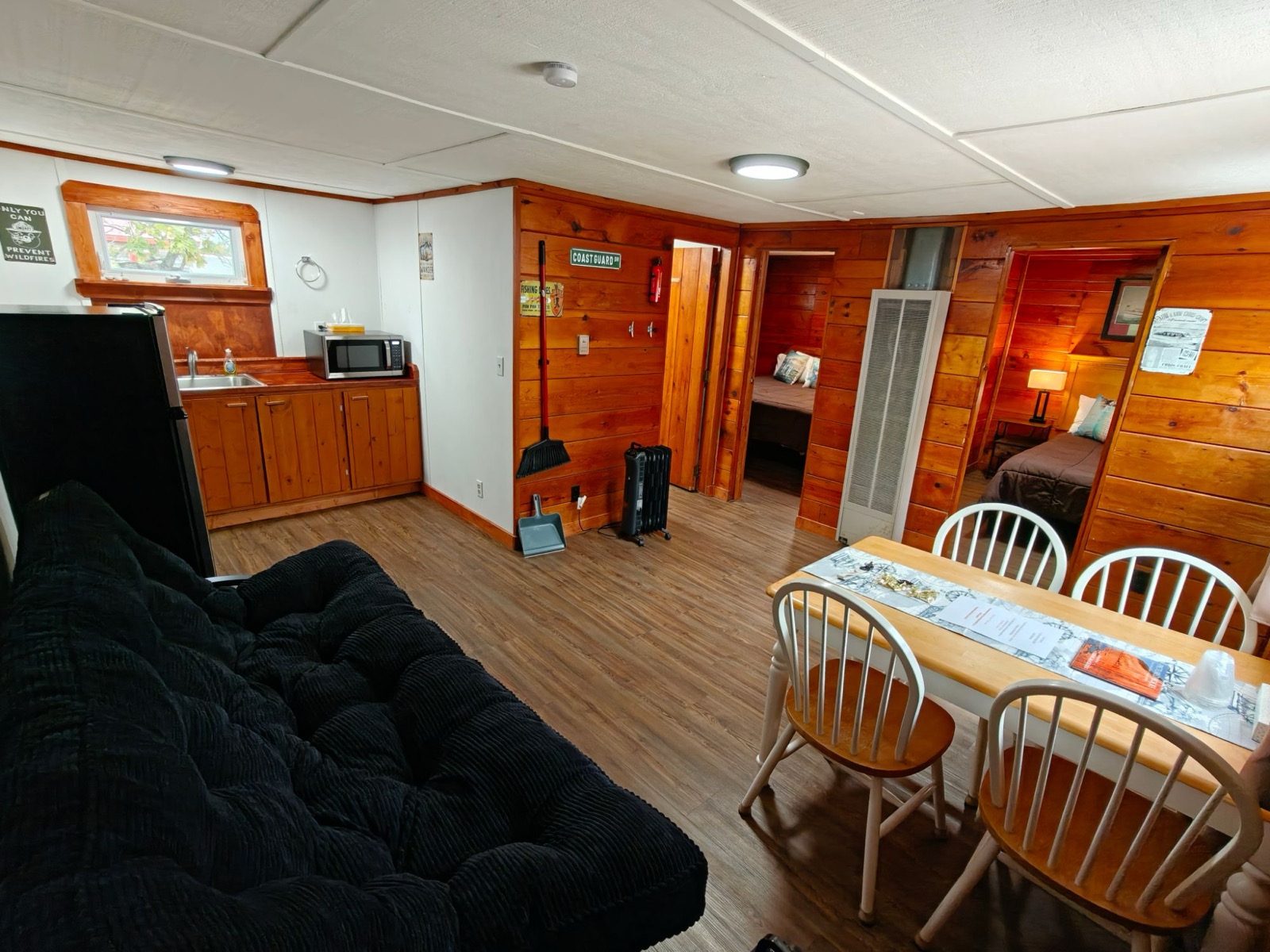 The living room: a futon, a kitchenette with a sink and microwave, a table for four and the doors to both bedrooms