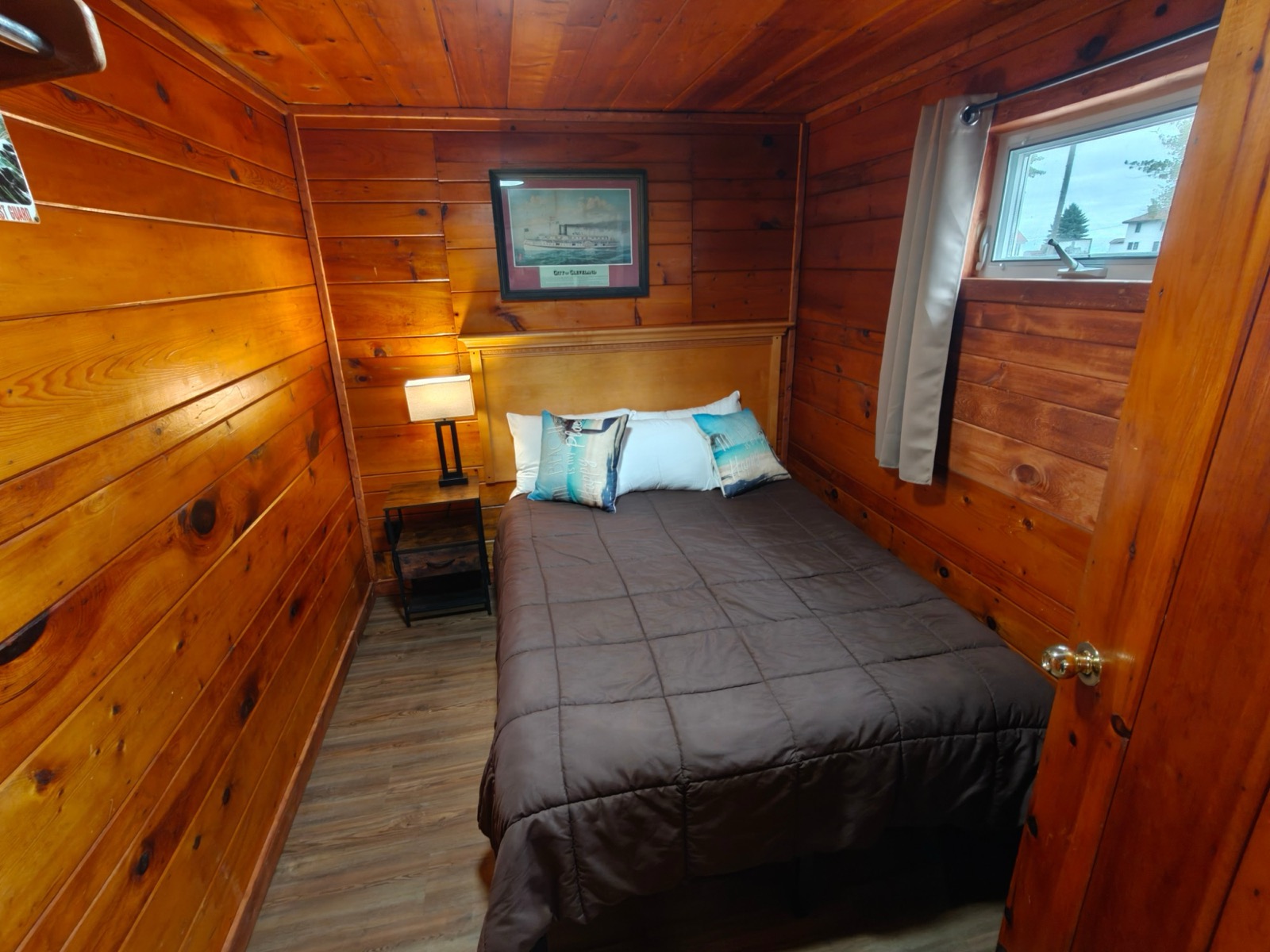 The second bedroom: a bed under a steamship print, a lamp lit and a window