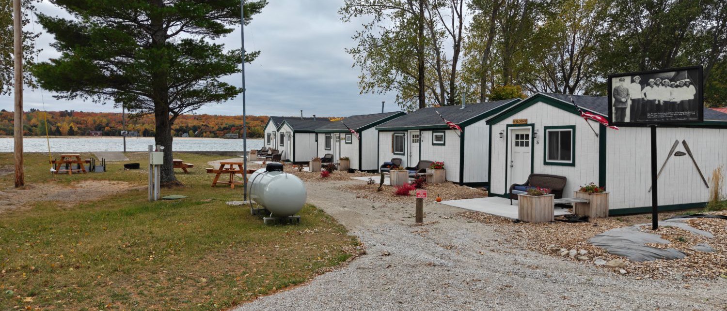 White cottages with green trim along a gravel lane, picnic tables on the grass and West Bay behind