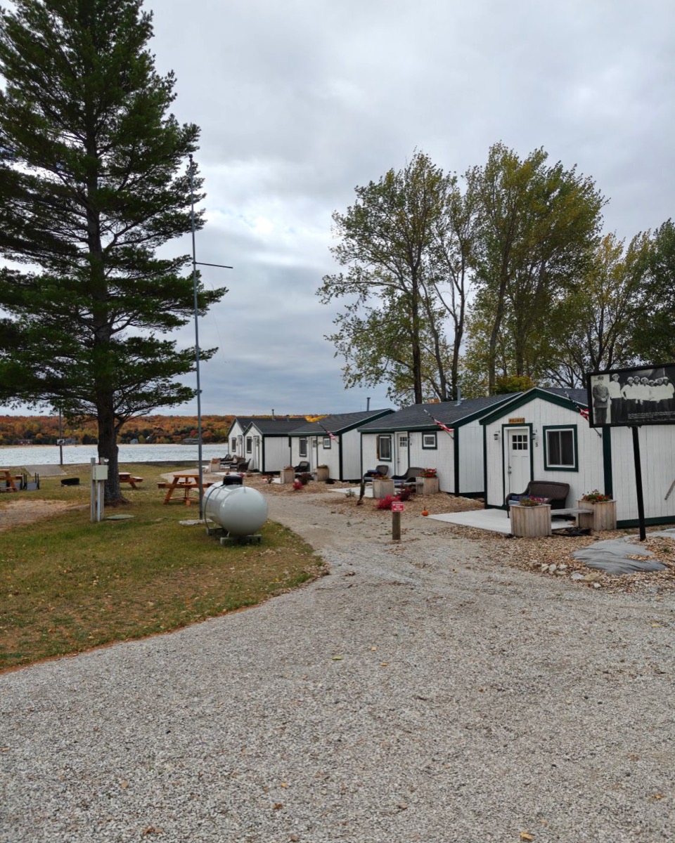 A row of white cottages with green trim along a gravel lane, West Bay and fall color behind