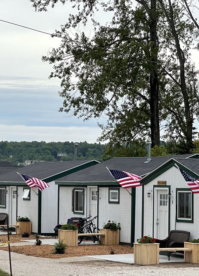 A row of white waterfront cottages with flags, porches and planters, West Bay behind