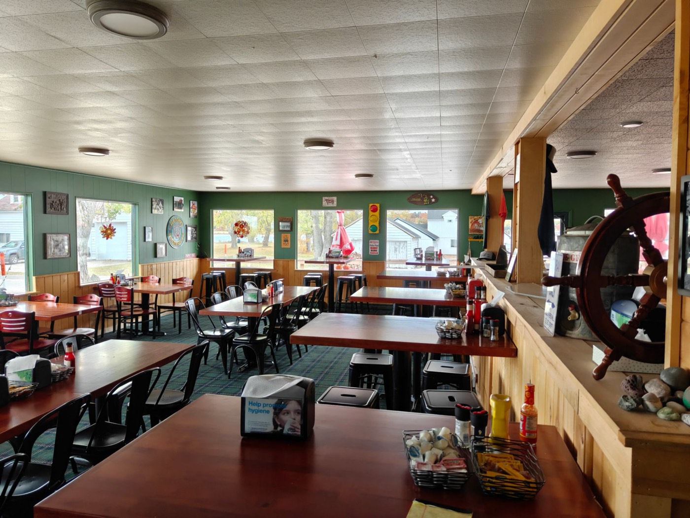 The dining room at Fletchy's: wooden tables, green walls, windows on the bay and a ship's wheel by the counter