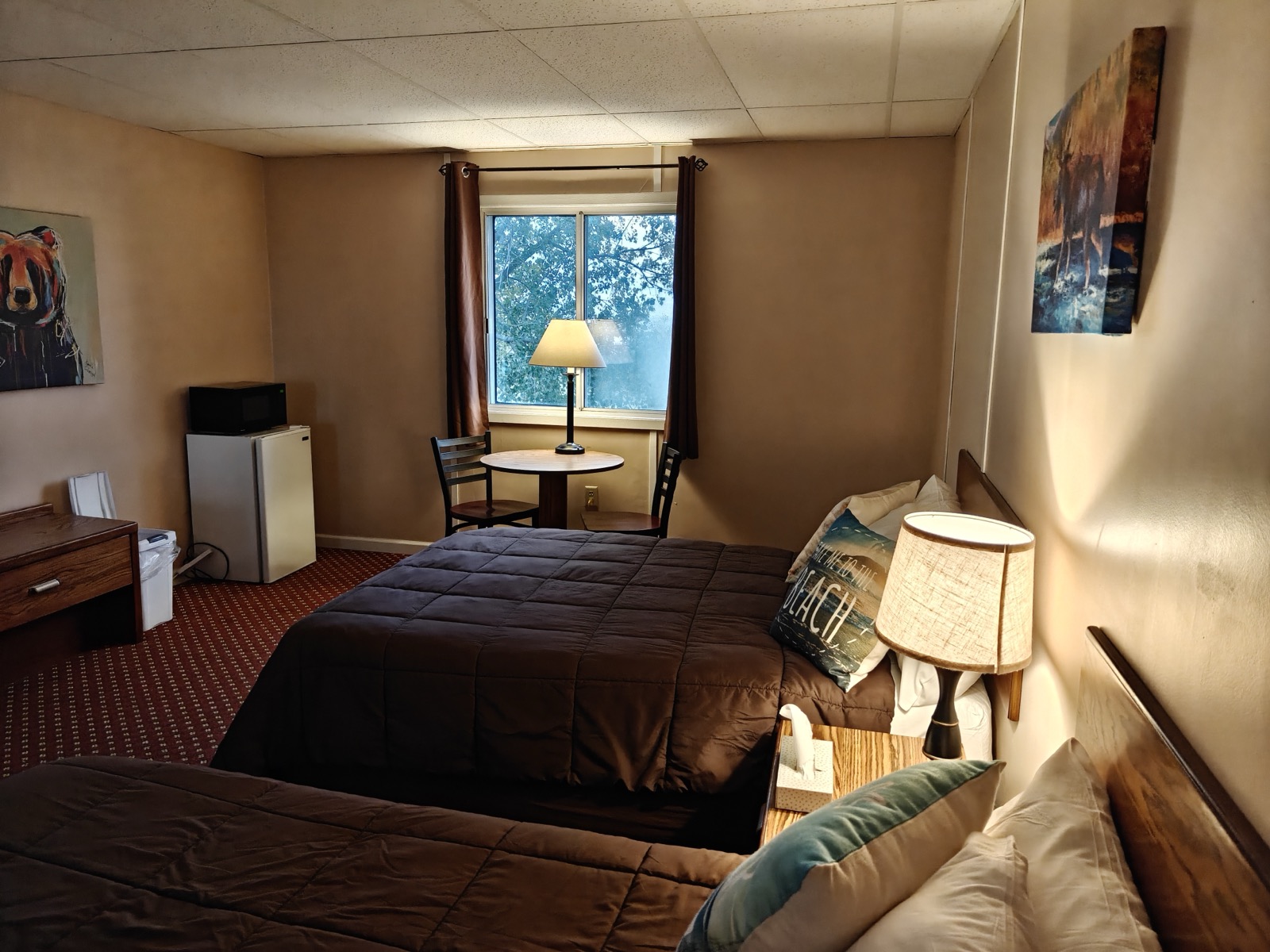 The table and chairs by the window, a lamp lit, the second bed alongside