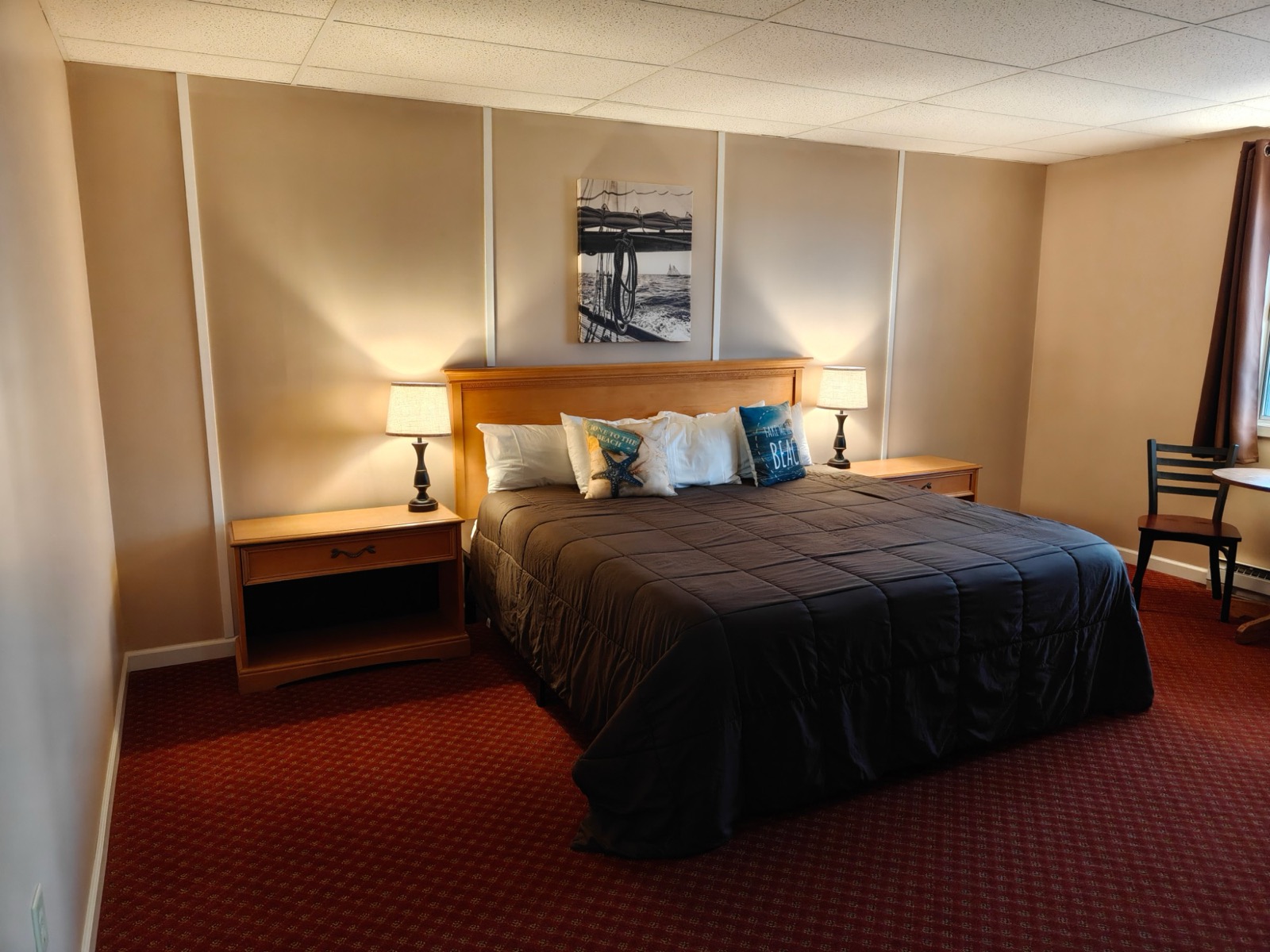 A motel King room: a king bed with white pillows and beach cushions, lamps on both nightstands and a sailing print above