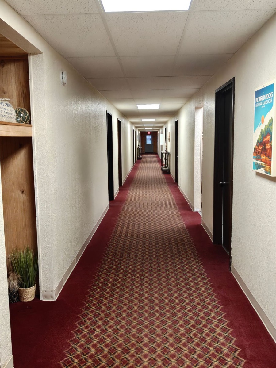 The motel hallway: a red patterned carpet, dark doors and a Pictured Rocks poster