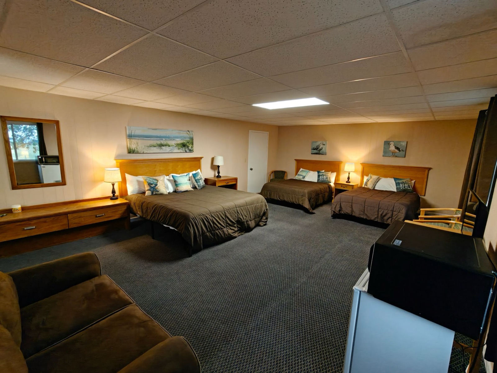 The suite: a king bed and two more beds, a sofa, a dresser with a mirror and beach art on the walls