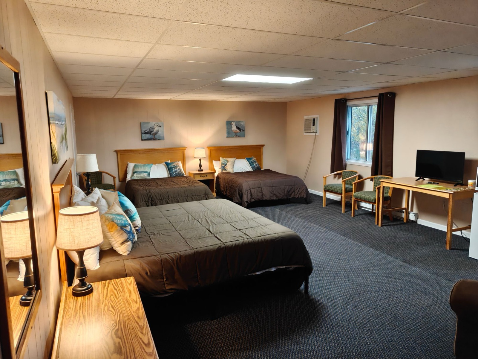 Three beds side by side, two armchairs by the window and a desk with a TV