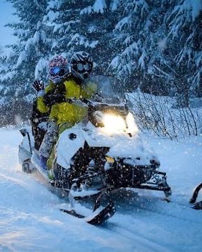 Two riders on a snowmobile in falling snow at dusk