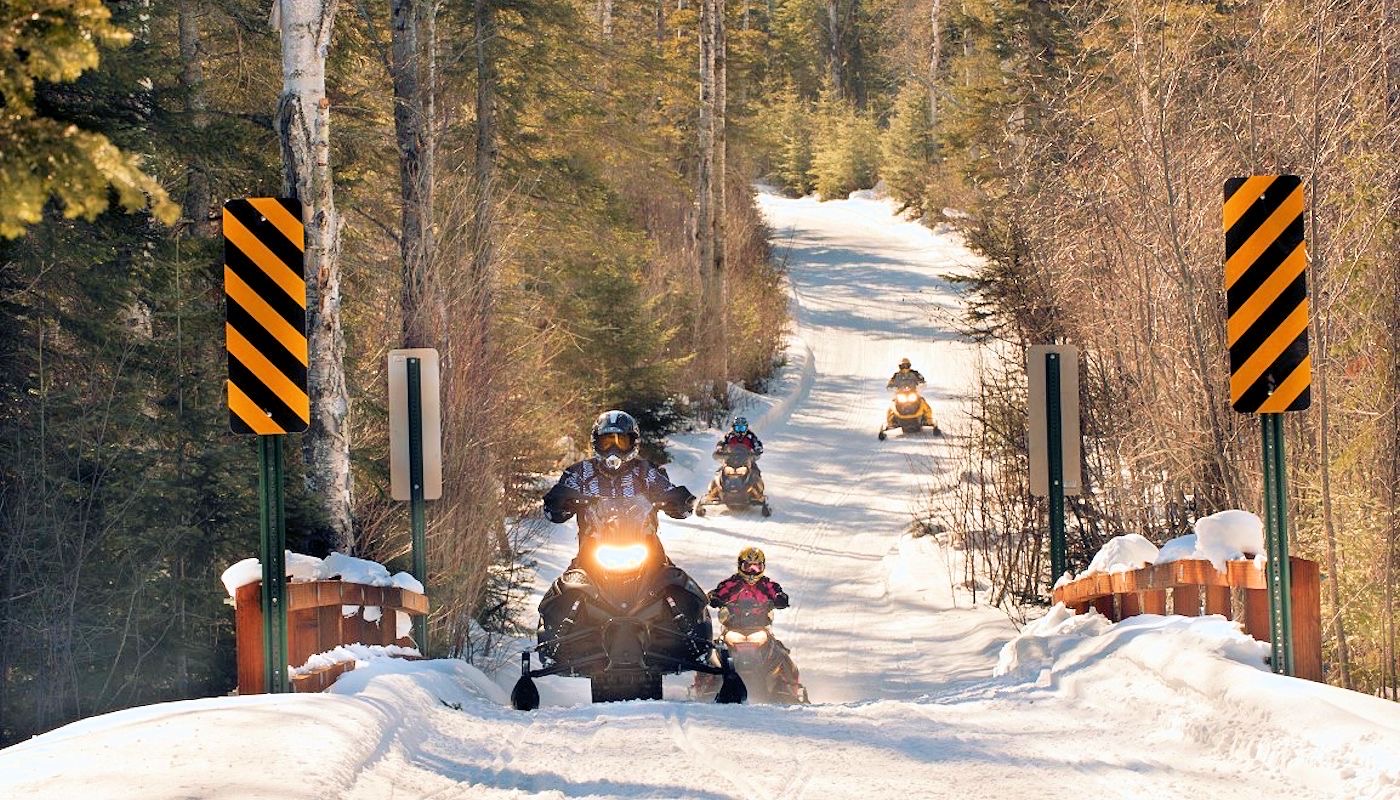 Snowmobiles crossing a wooden bridge on a forest trail