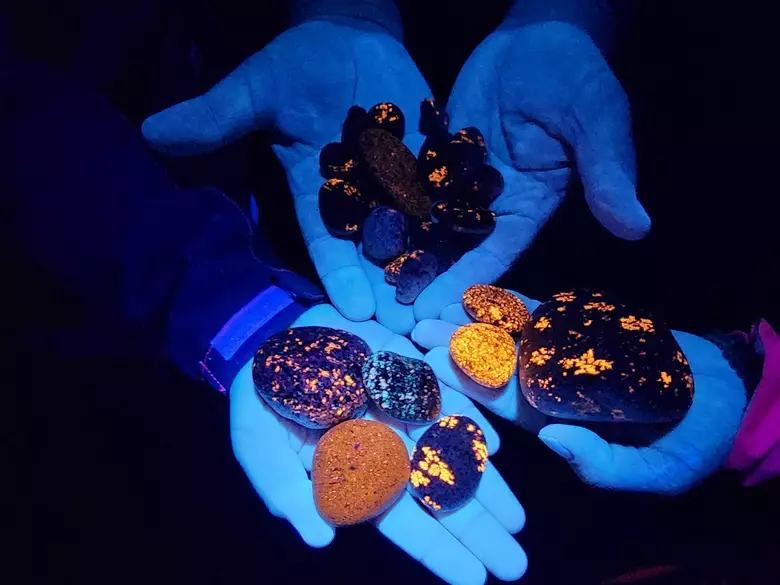 Yooperlites glowing orange under UV light in two hands